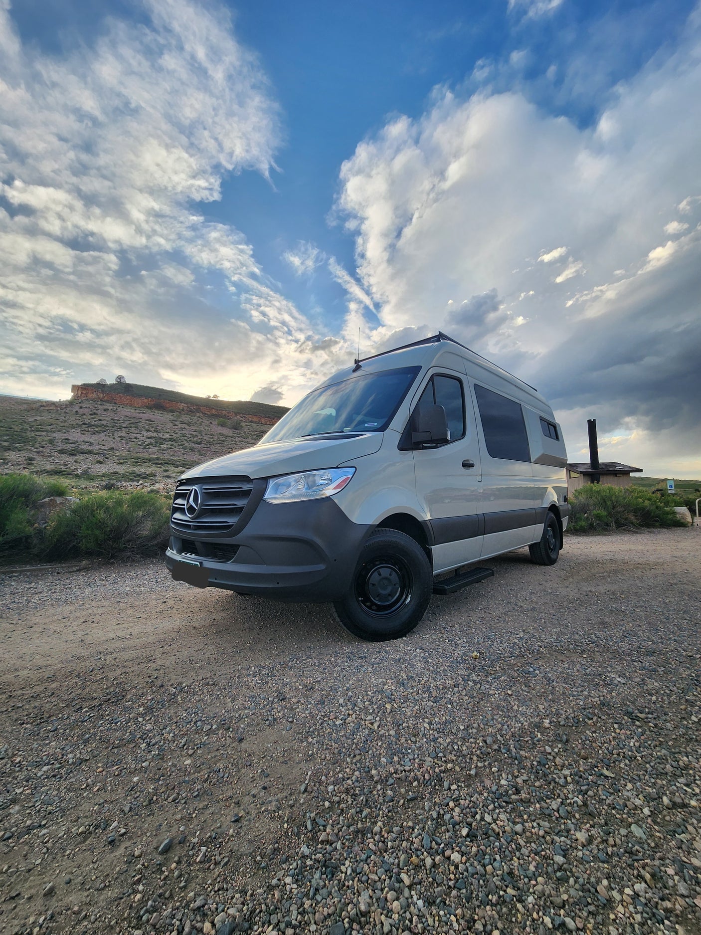 A light-colored Mercedes Sprinter camper van, ideal for RV rental adventures, parked on a gravel road by a mesa.
