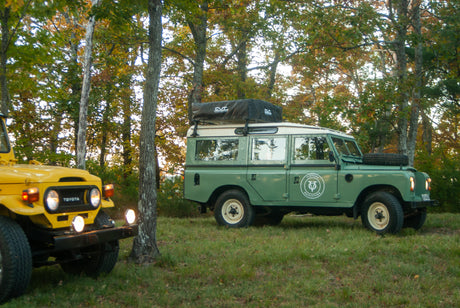 Yellow Toyota & green Land Rover with rooftop tent in woods. Perfect for an adventure RV rental.