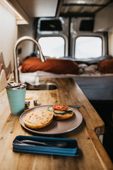 Cozy RV rental breakfast: a bagel with spreads & veggies, coffee, and a compact kitchen in a travel van.