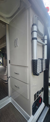 Inside an rv rental: sleek cabinets, storage drawers, and a space-saving ladder mounted on the wall, with utility controls below.