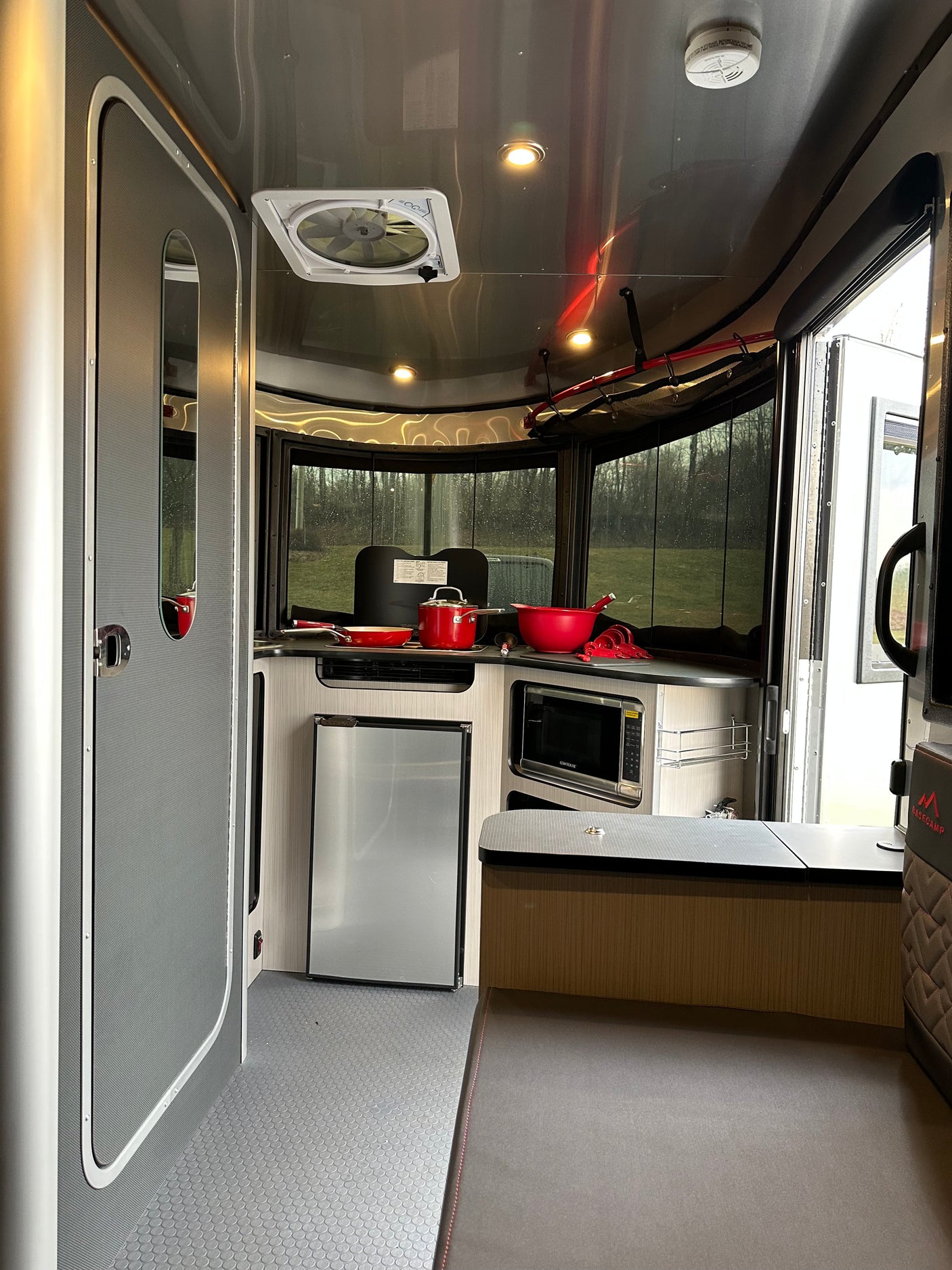 Modern RV rental interior with compact kitchen, fridge, microwave, and large windows revealing a scenic view. Perfect for adventures!