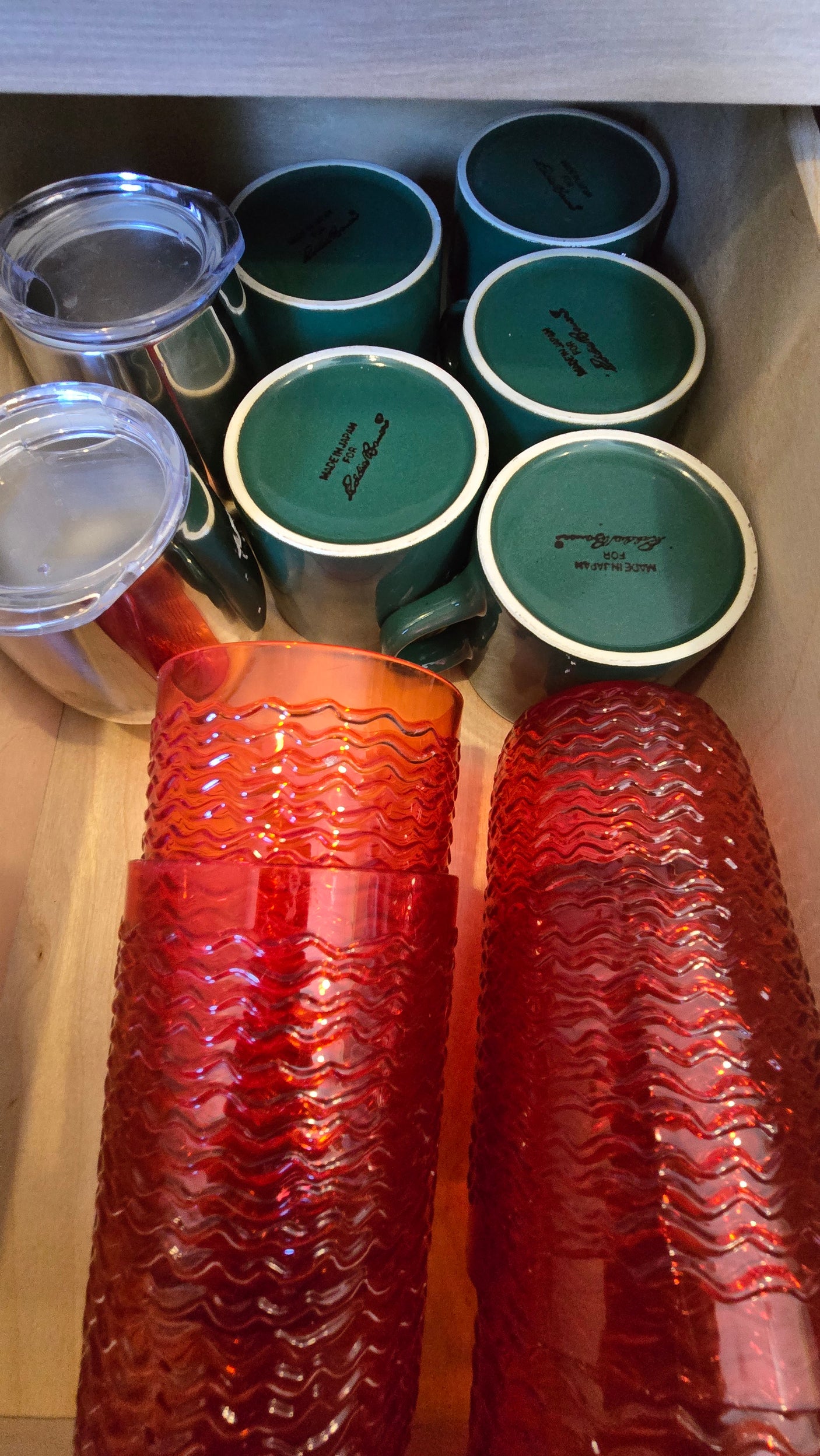Kitchenware drawer in an RV rental: green mugs, travel tumblers, and red textured cups neatly stored.