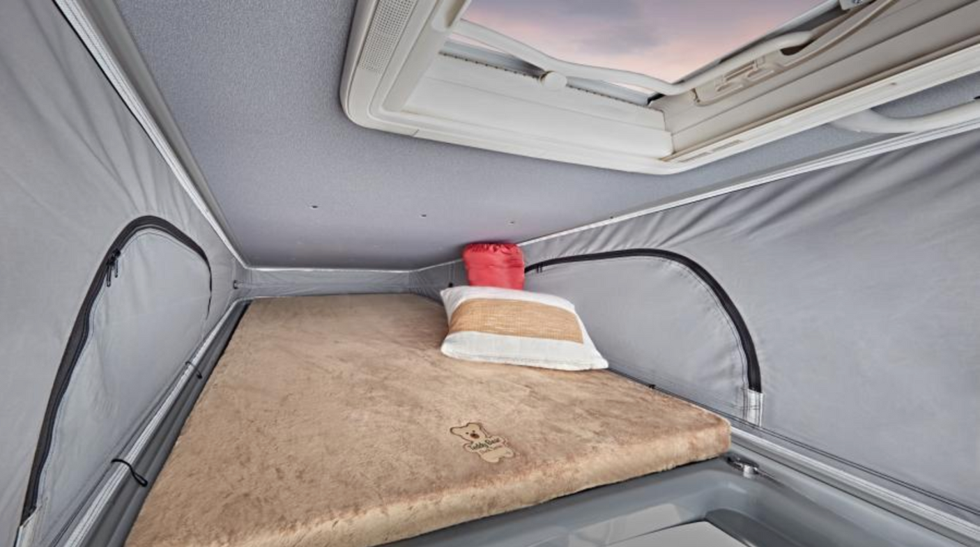 Cozy pop-top sleeping area in an RV rental. Features a fluffy bed, pillow, and skylight for travel comfort.