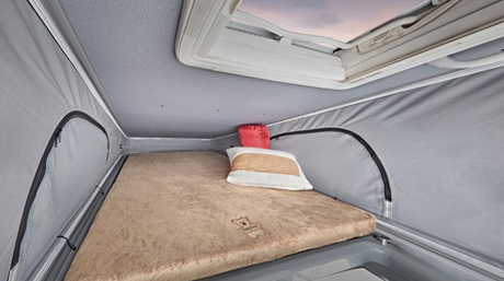 Cozy pop-top sleeping area in an RV rental. Features a fluffy bed, pillow, and skylight for travel comfort.