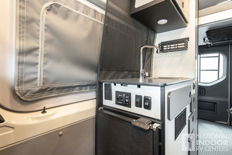 RV rental interior: compact kitchen with sink, Nova Kool fridge, control panel, and storage. Ideal for van adventures.