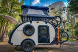 This sleek teardrop RV rental, featuring a rooftop tent and bikes, is set in a scenic forest campground with a mountain view.