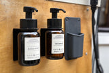 Compact RV rental bathroom essentials: wall-mounted hand soap and shampoo dispensers on a wooden wall, with a small holder.
