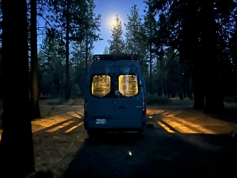  next to a bed with a colorful pillow.|RV rental interior wall: grey fabric with a timer switch (10-60 min) and an electrical outlet featuring USB ports.|RV rental: An open overhead cabinet reveals a control panel with a Victron battery monitor — photo 15