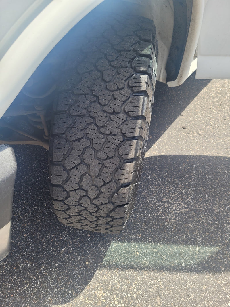 Close-up of an RV rental's all-terrain tire and wheel well on asphalt, showing the rugged tread pattern. — photo 3