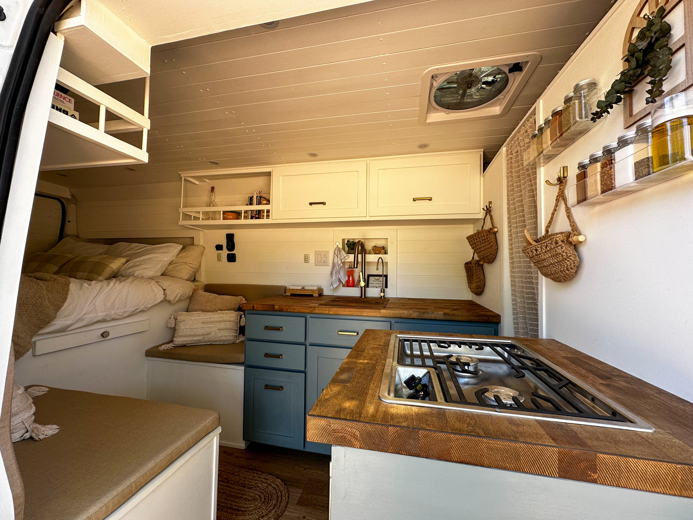 RV rental interior features a full kitchen with wood counters, light blue cabinets, cozy bed, and storage.