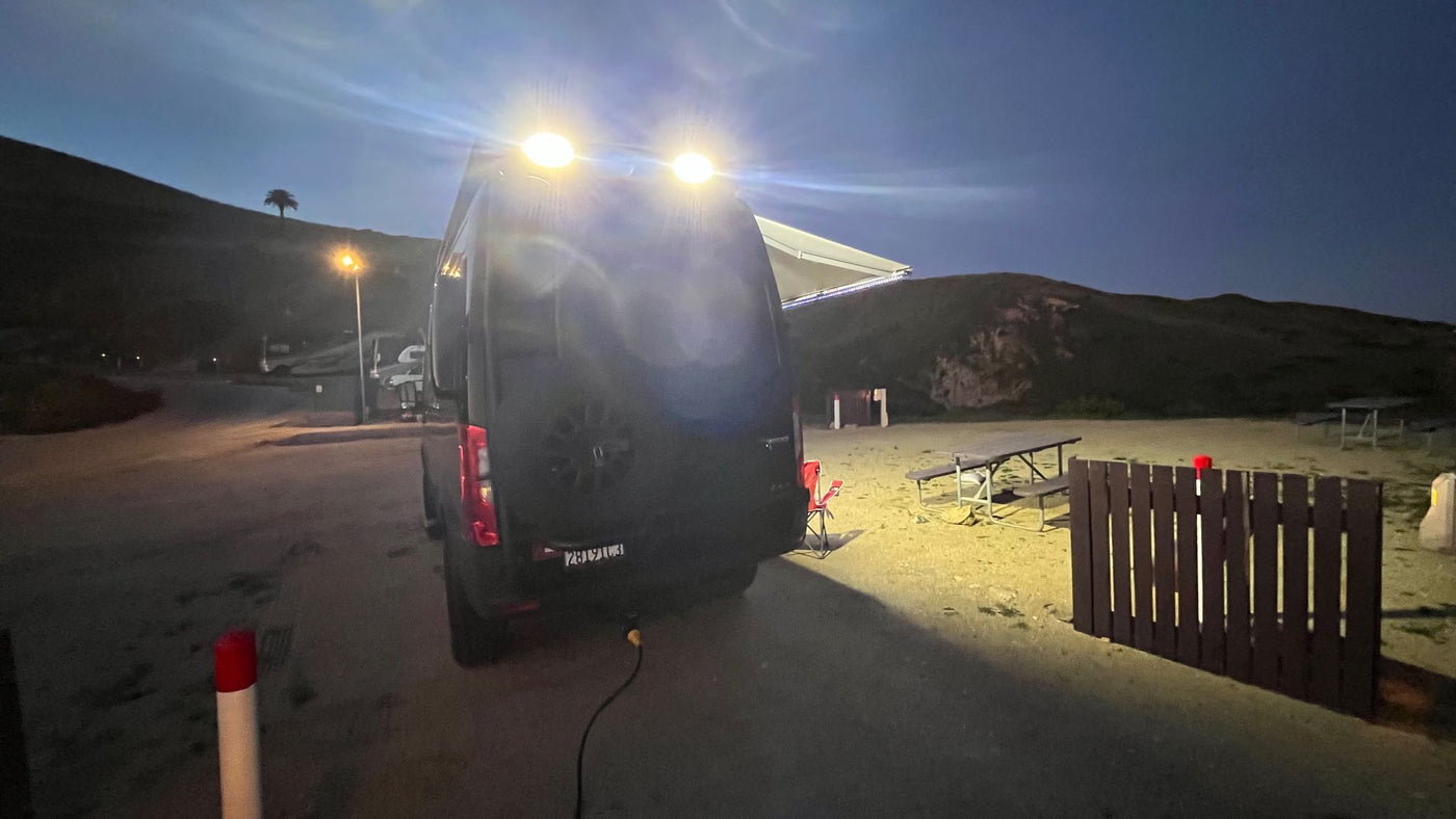 A dark RV rental shines bright lights at a nighttime campsite with picnic tables & hills, perfect for outdoor travel. — photo 17