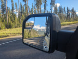 Scenic drive from an RV rental, showing road, pine forest, snowy mountains, and a side mirror reflection.