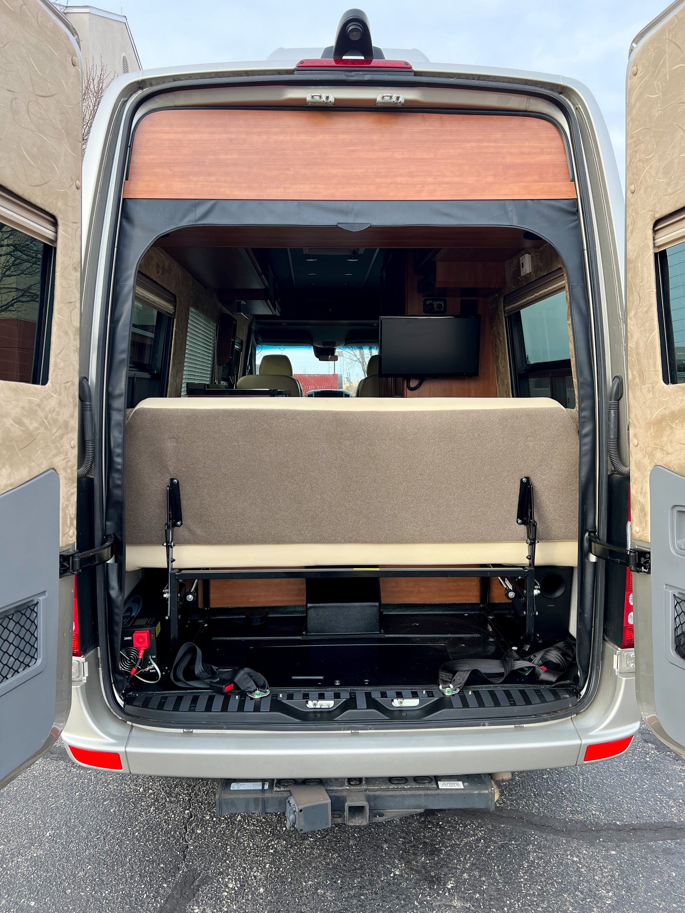 Rear view of an RV rental's interior, showing a convertible bed/lounge, TV, and hitch receiver.
