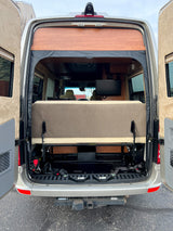 Rear view of an RV rental's interior, showing a convertible bed/lounge, TV, and hitch receiver.