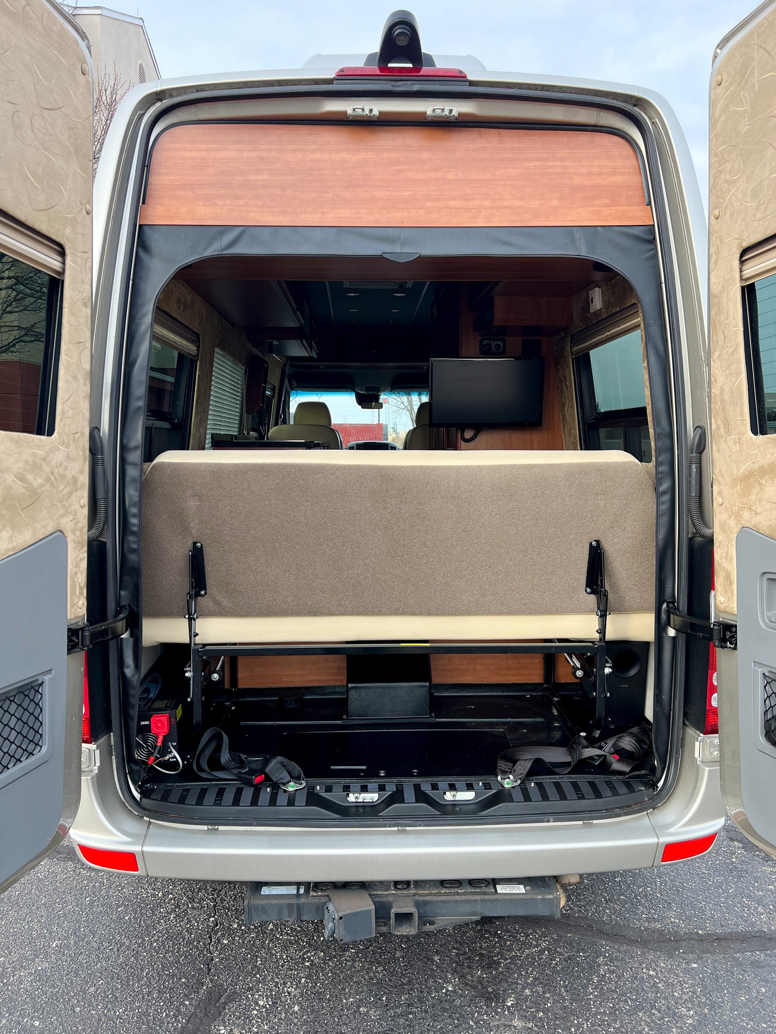 Rear view of an RV rental's interior, showing a convertible bed/lounge, TV, and hitch receiver.