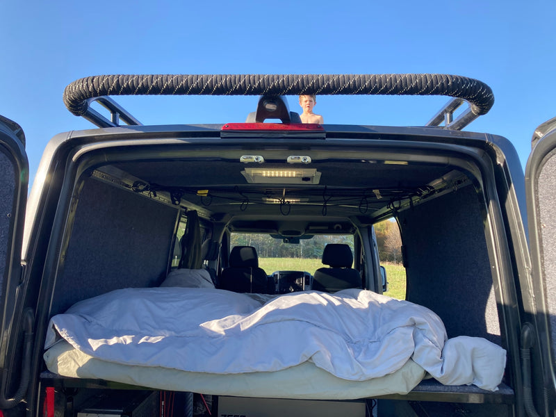 Inside a spacious RV rental van: a comfy bed, open doors to nature, and a child peeking from the roof rack. Ready for adventure! — photo 15