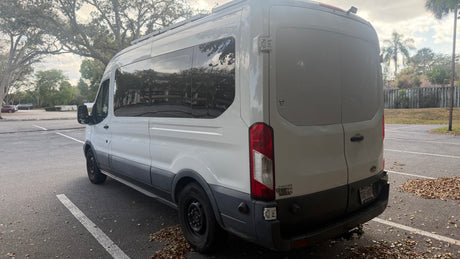 Rear view of a white Ford Transit van, a popular rv rental option, parked in an outdoor lot. Shows windows, license plate.