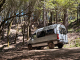 White Mercedes Sprinter rv rental van parked in a sun-dappled forest, nestled among tall, mossy trees.
