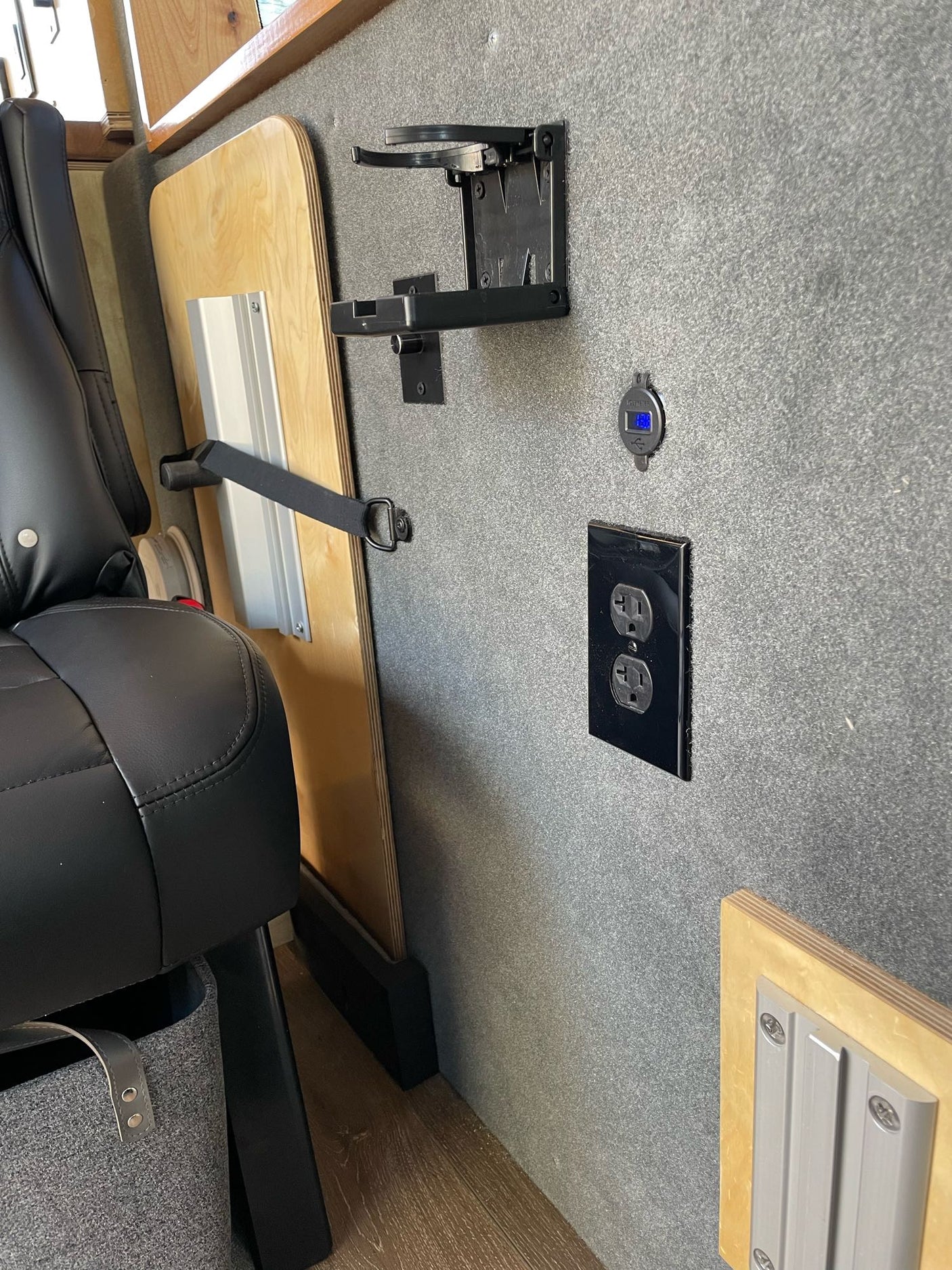 RV rental interior featuring a black leather seat, stowed wooden table, USB charging port, and AC outlet on a grey wall.