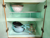 RV rental kitchen cabinet with neatly organized blue pots, pans, lids, & colanders on shelves.