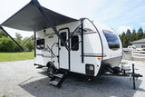 Modern white travel trailer RV with black accents and extended awning on gravel. Ideal for RV rental trips.
