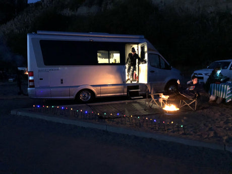 Enjoying an RV rental adventure: An Airstream campervan at night with people by a cozy campfire, illuminated for outdoor relaxation.