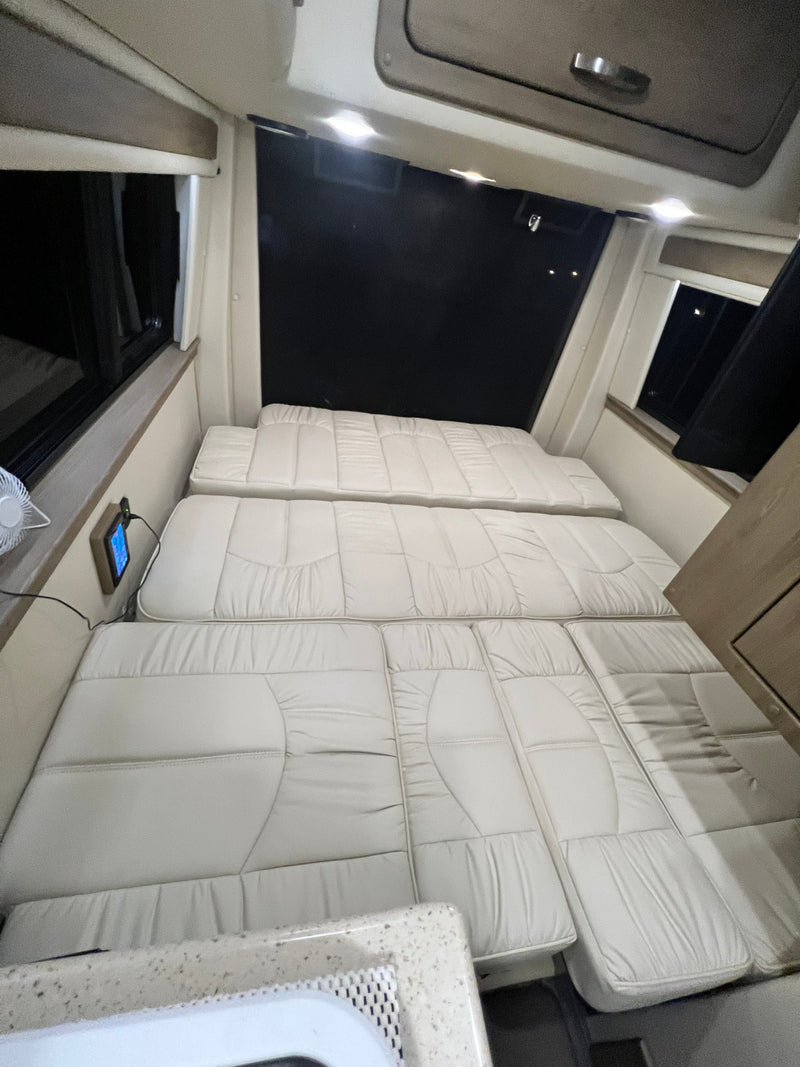 Spacious RV rental interior featuring light-colored cushions arranged as a bed, with windows & control panel access. — photo 8