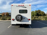 Rear view of a white Majestic RV rental with an 'I ❤️ CAMPING' tire cover, parked in a sunny lot.