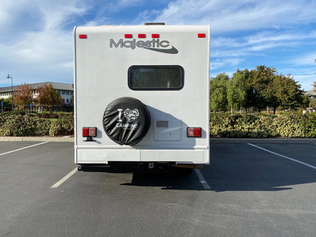 Rear view of a white Majestic RV rental with an 'I ❤️ CAMPING' tire cover, parked in a sunny lot.
