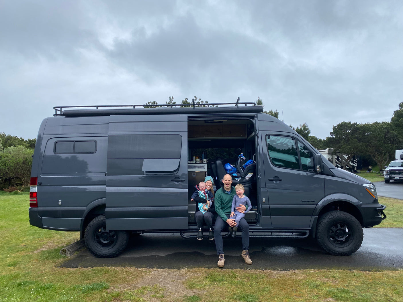 Family enjoying their RV rental, a dark grey camper van, at a campsite. Perfect for family travel.