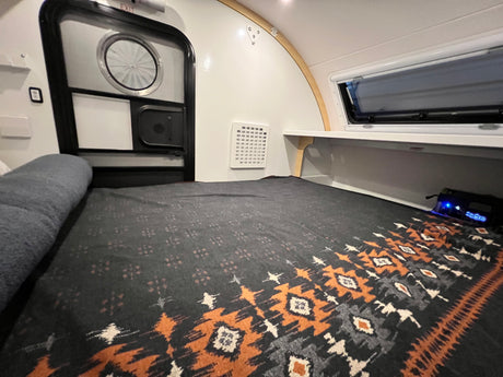 Cozy RV rental interior: a comfortable bed, entrance door, wall vent, and side window for compact travel.