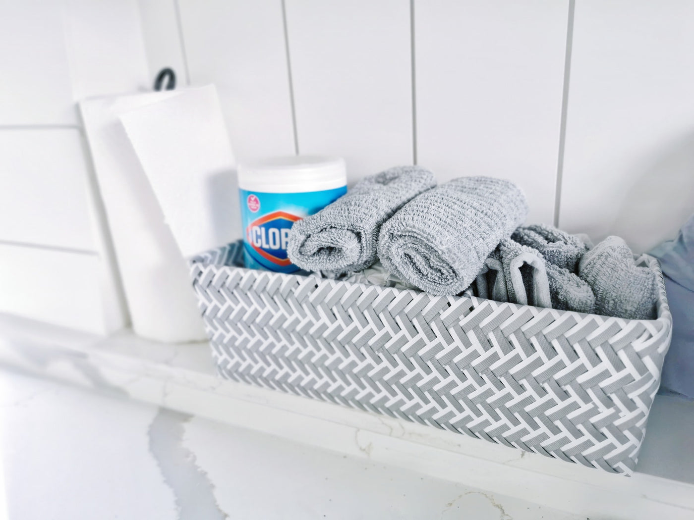 Organize your RV rental: woven basket with rolled grey towels, Clorox wipes, and paper towels on a white counter. — photo 20