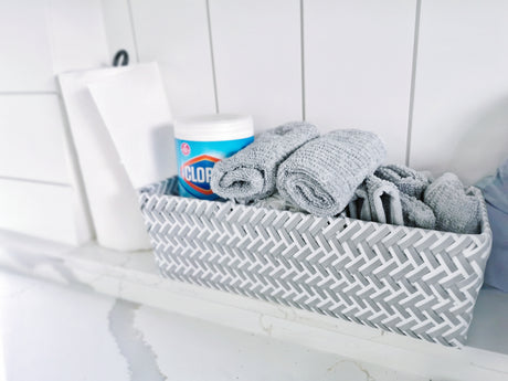 Organize your RV rental: woven basket with rolled grey towels, Clorox wipes, and paper towels on a white counter.