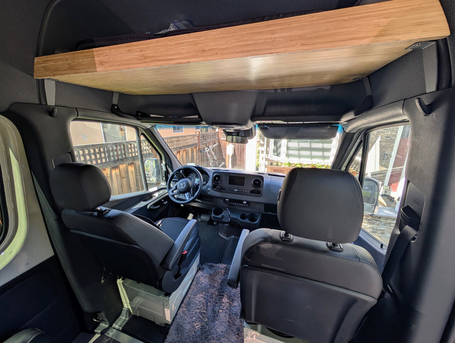 Inside a custom Mercedes Sprinter van conversion: comfy seating, overhead wood storage/bunk. Ideal for your RV rental getaway!