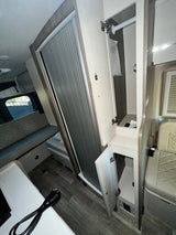 RV rental interior featuring a wardrobe with hanger, a retractable door, open storage cabinets, and quilted bench seating.