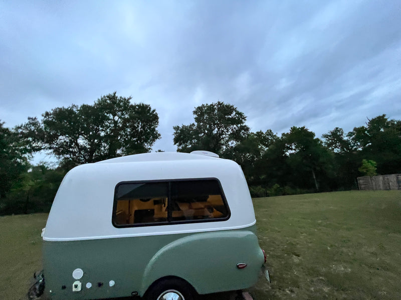 Compact, retro RV rental trailer with white & green exterior, parked in a grassy field under an overcast sky. — photo 7