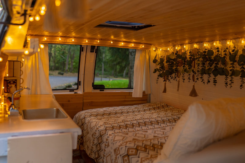 Cozy RV rental interior with bed, kitchen, string lights & hanging plants, perfect for van life adventures. — photo 14