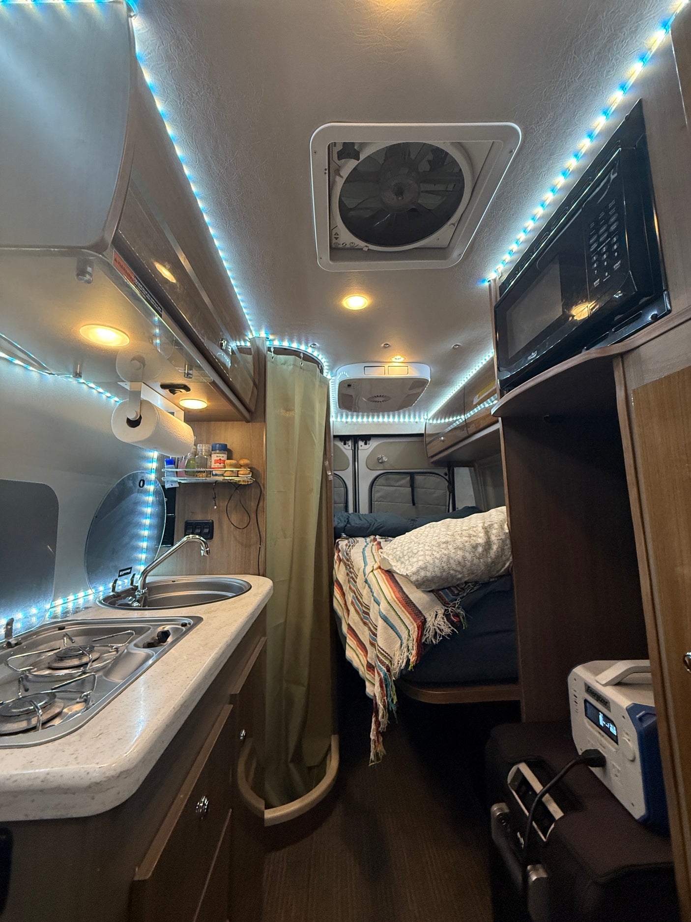 Cozy RV rental interior: well-equipped kitchen, comfortable bed, microwave, and bright LED lights. Ideal for adventures!