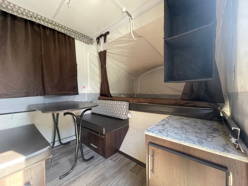 Interior of an RV rental pop-up camper, featuring a dining nook, bed, and compact kitchen area. — photo 6