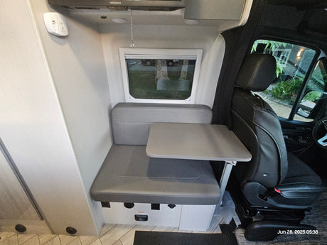 RV rental interior: Cozy dinette with grey cushions, table, and passenger seat view in a camper van.