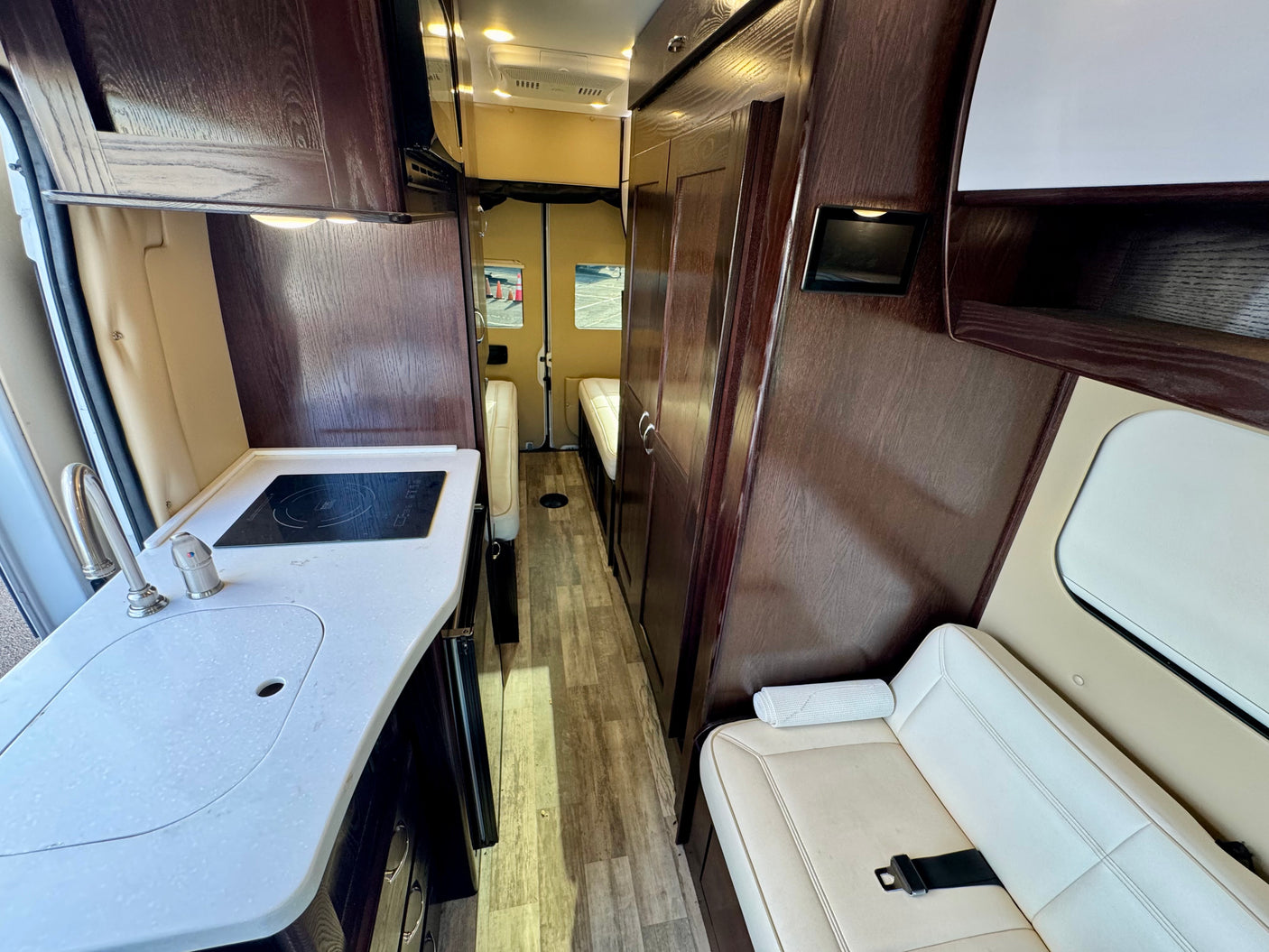 Step inside this modern RV rental! Features include a well-equipped kitchen with a sink and cooktop, sleek wood cabinetry, and cozy seating.