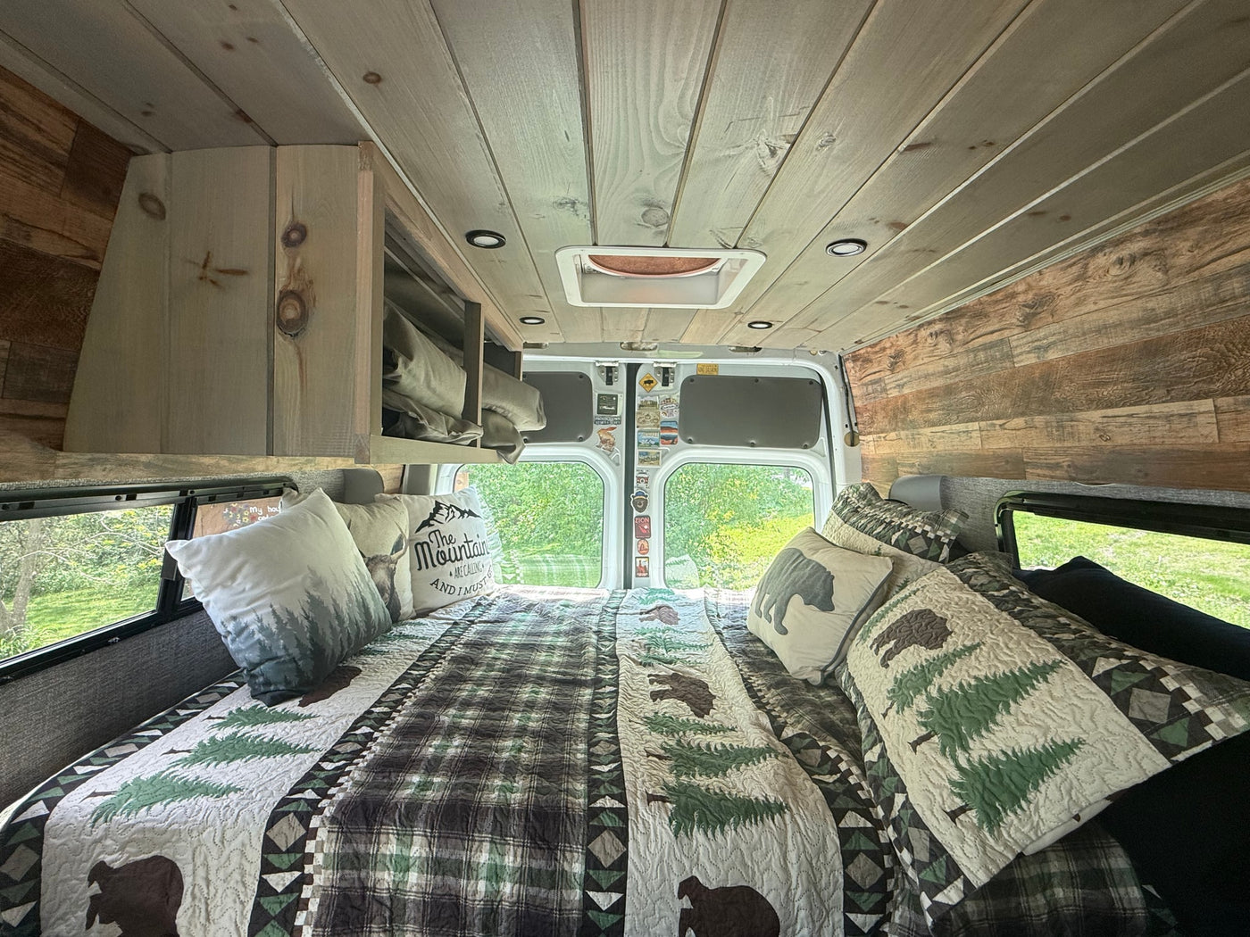 Cozy RV rental camper van bedroom with rustic wood paneling, woodland-themed bedding, and scenic windows. — photo 8