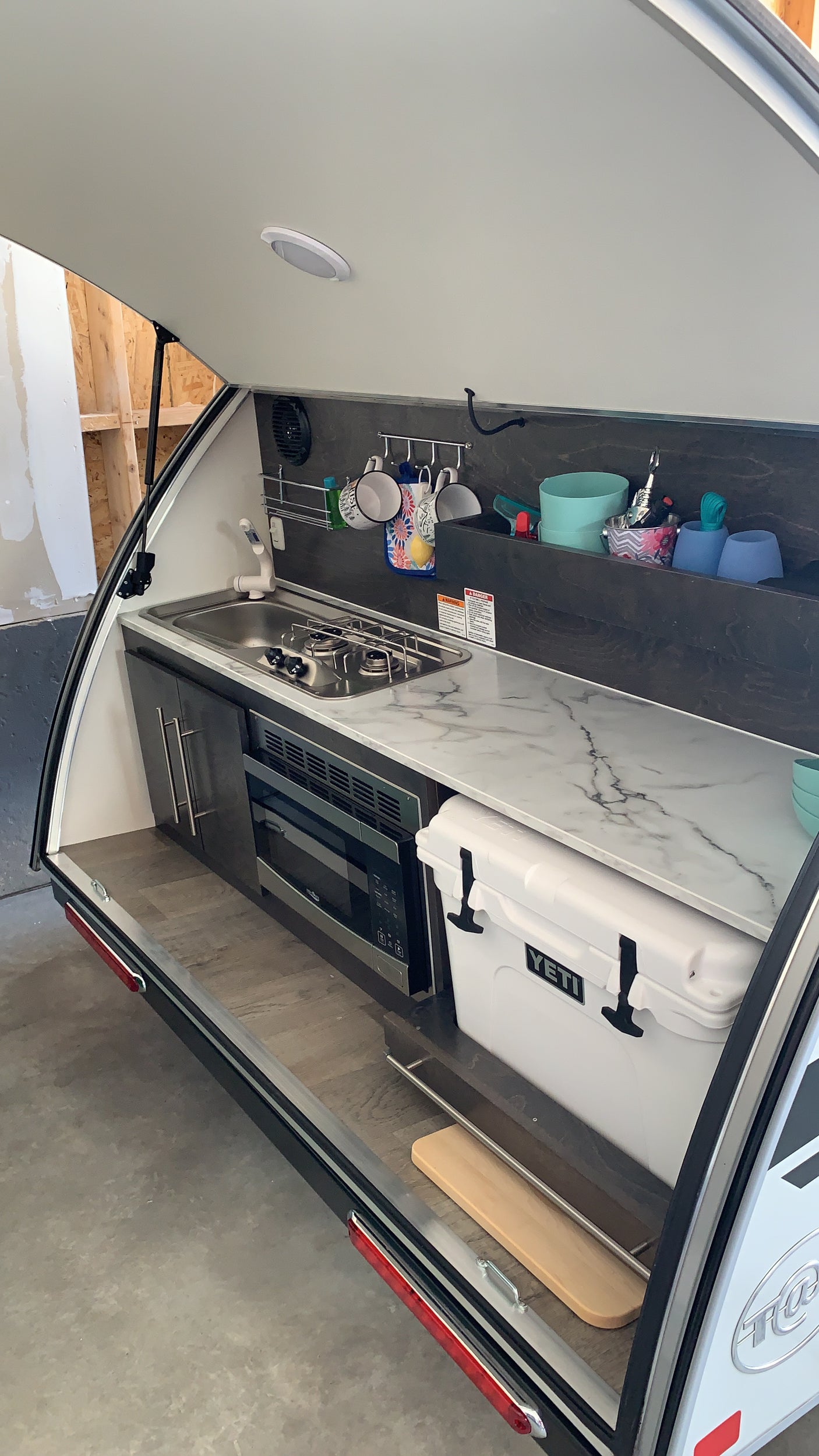 RV rental's open rear galley kitchen, featuring a sink, stove, microwave, and Yeti cooler for convenient outdoor cooking.