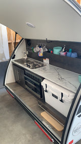 RV rental's open rear galley kitchen, featuring a sink, stove, microwave, and Yeti cooler for convenient outdoor cooking.