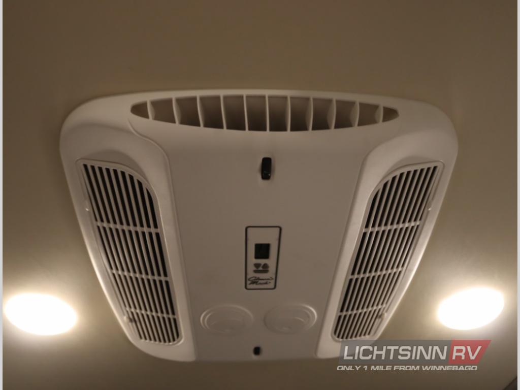 Overhead view inside an RV rental, showcasing the central air conditioning unit with vents and two bright ceiling lights for comfort.