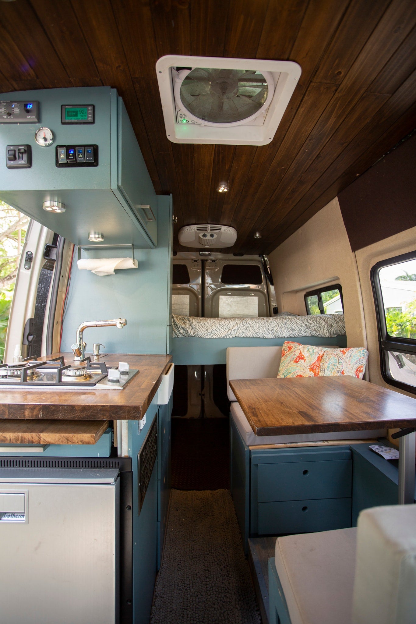 RV rental interior featuring a functional kitchen with stove and sink, cozy bed, dining area with table, and control panel. — photo 2