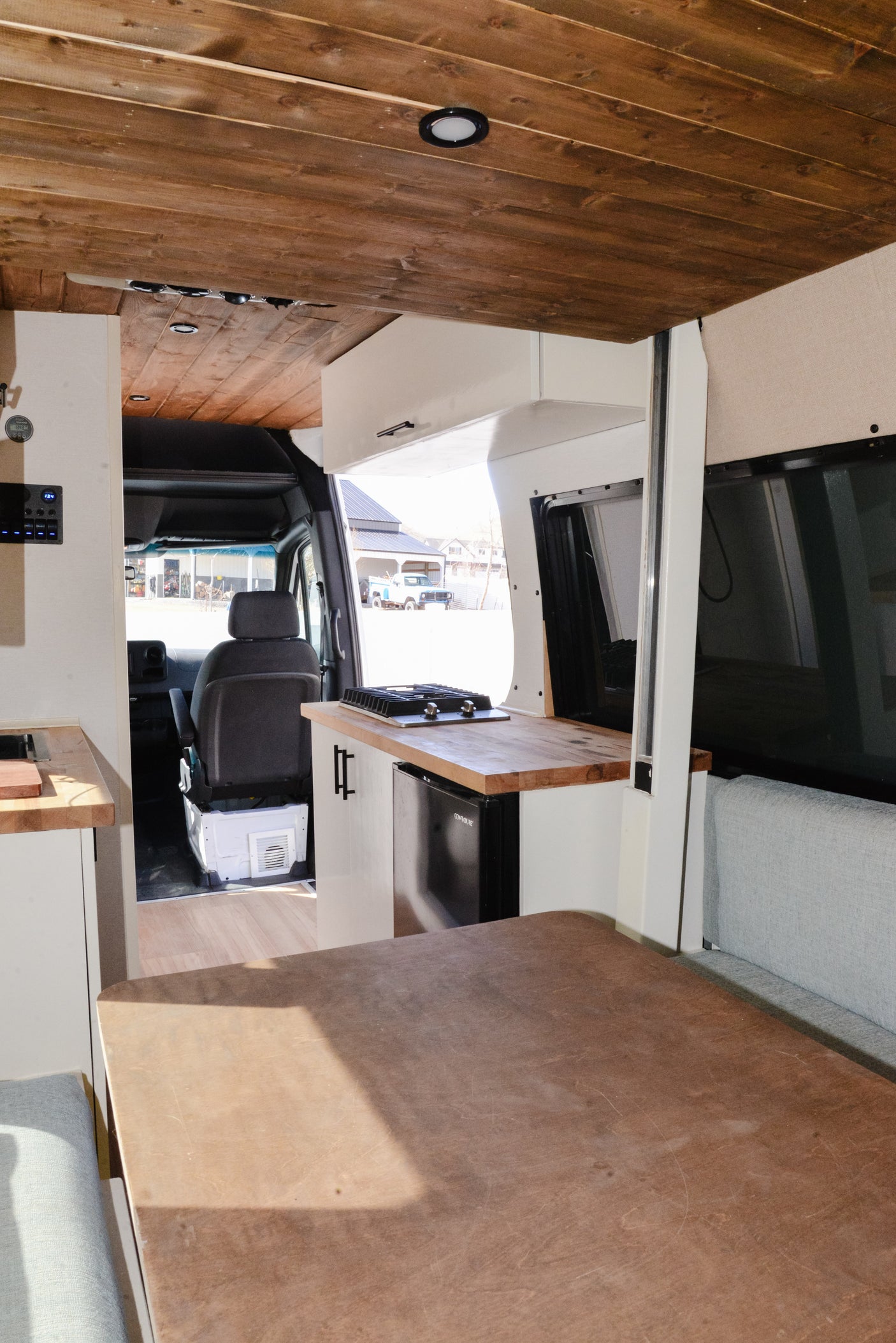 Modern RV rental interior with a wooden plank ceiling, kitchenette, fridge, and a large dining table. Ready for your next trip!