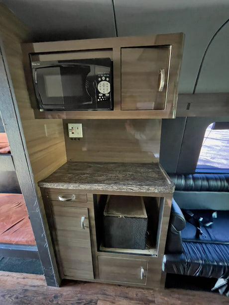 This RV rental's compact kitchenette features a microwave, stone-look counter, cabinets, outlets, and visible bunks.