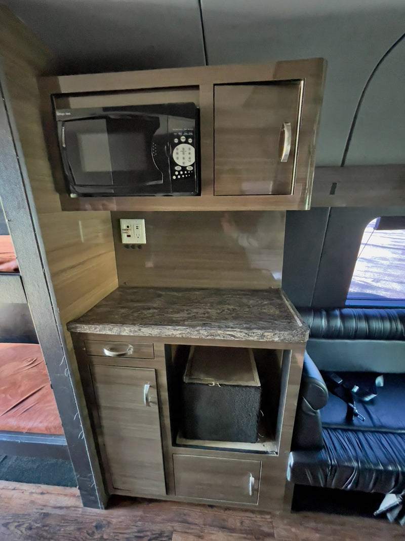 This RV rental's compact kitchenette features a microwave, stone-look counter, cabinets, outlets, and visible bunks. — photo 19
