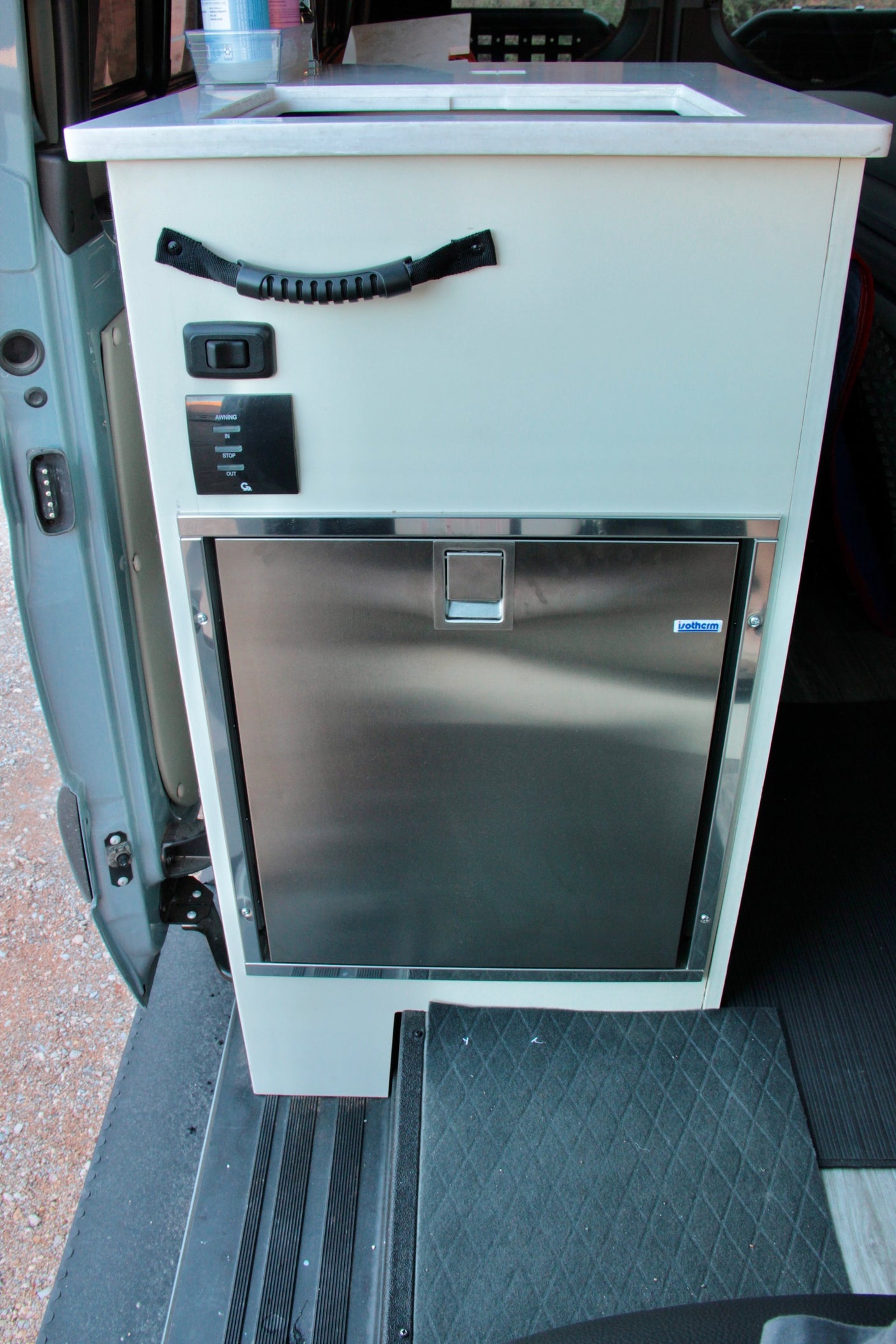Inside this RV rental: A compact, light-colored cabinet houses a sink, Isotherm fridge, and awning controls.